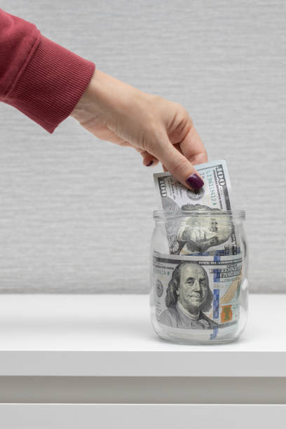 istock man puts one hundred dollar bill in a glass jar 1464394700