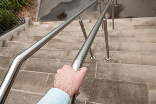 A man's hand on the railing of outdoor concrete stairs.