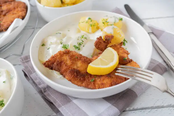 Delicious homemade dinner or lunch with fresh breaded chicken schnitzel. Served with kohlrabi and bechamel sauce and boiled potatoes on a plate. Closeup