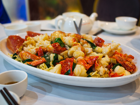 A large plate of stir-fried lobster lace with spring onions, ginger, garlic and noodles.