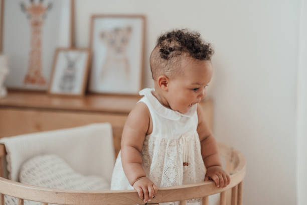 Portrait of mixed race toddler girl in round wooden baby crib at cozy childrens room neutral tones