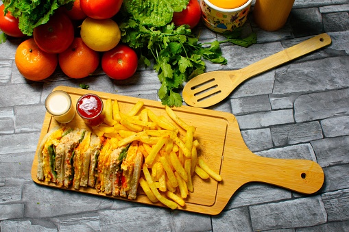 A top view of sandwiches and fried fries with sauce served on a wooden chopping board