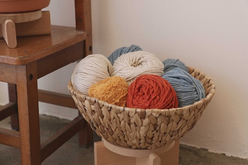 A closeup of colorful yarn balls in a basket on a chair indoors