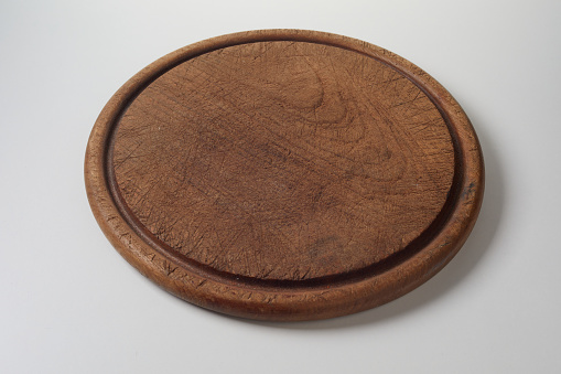 A from above round shaped wooden board for hot dishes serving covered with scratches and placed on gray table