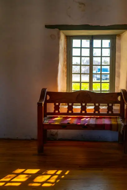 Photo of Sunrays over the empty benches and the window inside the chapel of Mission Espada, Missions National Historical Park in San Antonio, Texas, USA
