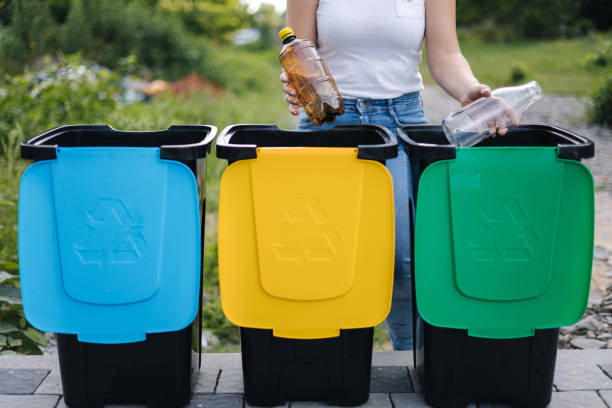 istock Middle selection of female hold two different bottle, plastic and glass and thowing into different recycling bins. Close-up of woman stand by blue, yeallow and green bin 1464410152