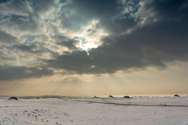 A scenic view of bright sunlight passing through clouds shining over a snow-covered field