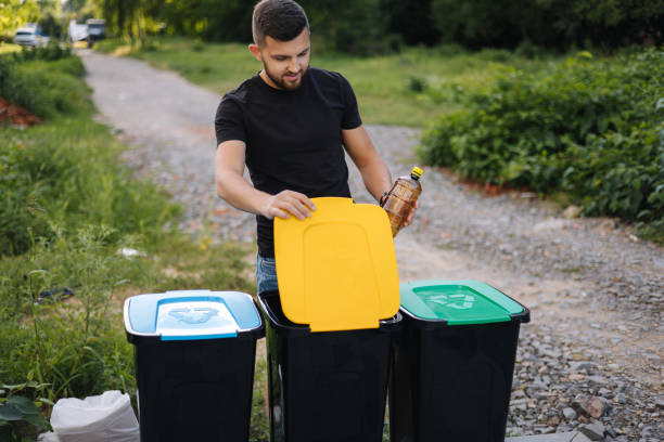 istock Man throwing plastic bottle into recycling bin on back yard. Different colours on plastic bins. Green, blue and yellow 1464412050