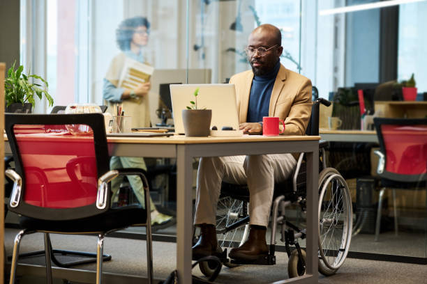 istock Young businessman sitting in wheelchair by table and networking 1464415896