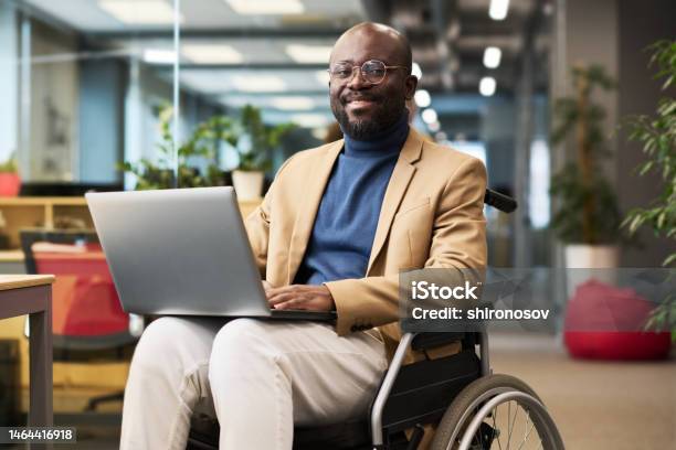 Happy Young Black Man With Disability Sitting In Wheelchair In Office Stock Photo - Download Image Now