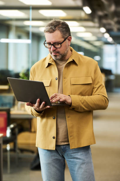 istock Serious mature businessman using laptop in openspace office 1464417810
