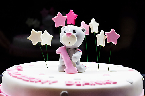 A selective of a birthday cake with a teddy bear holding the number 1