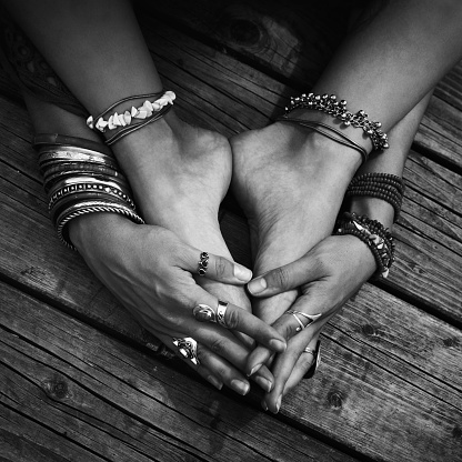 closeup of girl feet and hands with lot of boho style bracelets, rings outdoor on wooden background black and white close up