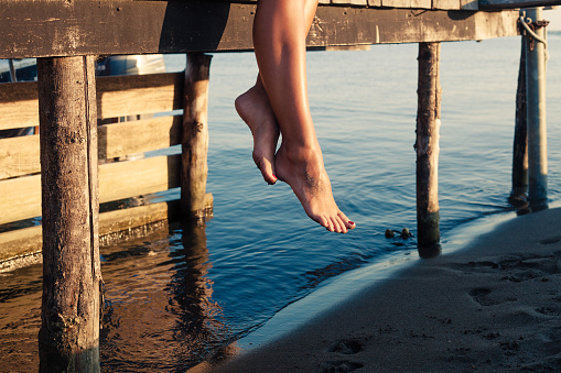 woman legs as she sitting on old wooden dock at sea shore close up
