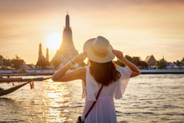 uma mulher aprecia a vista do pôr do sol para o famoso templo wat arun em bangkok - arun - fotografias e filmes do acervo