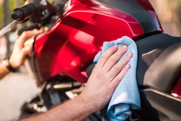 Photo of Closeup of a man cleaning a modern motorcycle with a towel outdoors