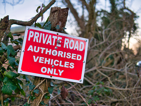 A prominent sign of white words on a red background in a hedgerow advises that the road ahead is private with access restricted to authorised vehicles only.