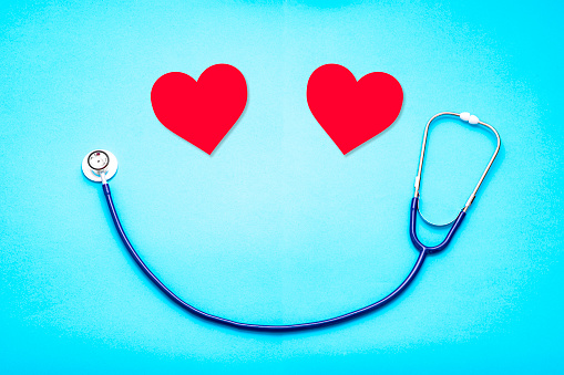 Top view of two hearts and a stethoscope making a smiling face shape against a light blue background