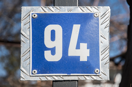 Weathered grunge square metal enameled plate of number of street address with number 94 closeup