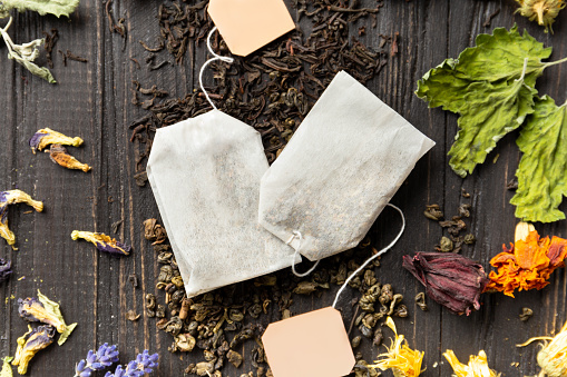 Composition of dry black and green tea, tea bags and dry hibiscus, calendula, lavender flowers on a dark wooden background top view close-up. Different types of dry tea on a dark background.