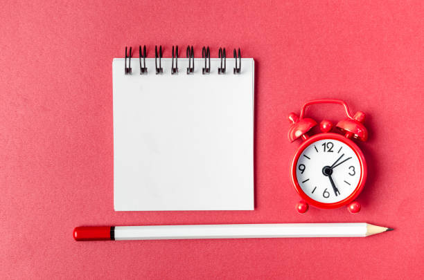 istock The Top view of open empty spiral notebook and alarm clock with pen on red background. 1464456519