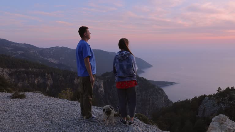 4k video of a couple with dog contemplating scenic view of Turkey sea from above during sunset