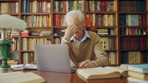 istock Senior man translator rubbing tired eyes, working long hours on laptop, writer 1464459388