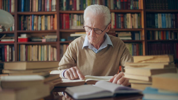 istock Mature man in eyeglasses reading interesting book, sitting in the library, studying 1464459527