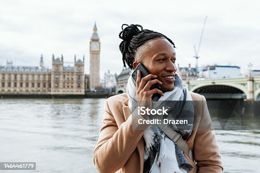 istock Young African man using smart phone, having a phone call. Braided African man standing near Big Ben in London, UK 1464461779