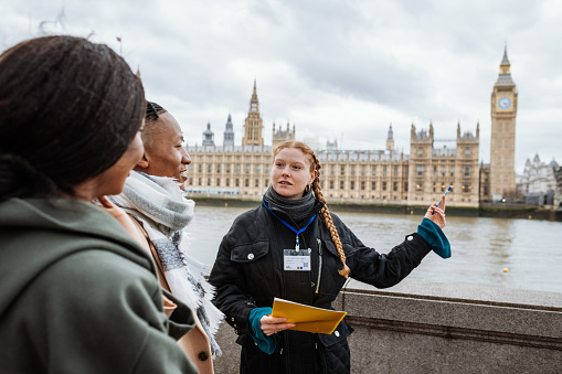 Young tourists in London, followed by private tour guide, showing them Parliament and Big Ben