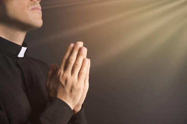 luz sagrada y sacerdote rezando sobre fondo negro, primer plano. espacio para texto - sotana fotografías e imágenes de stock