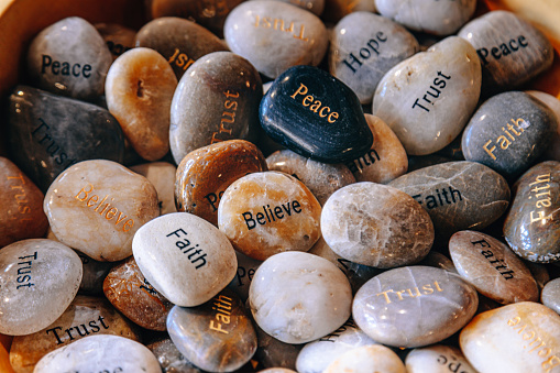 A pile of colorful engraved stones with a different word painted on each. Peace, Hope, Dream, Trust, and Believe on River Rocks  for inspiration