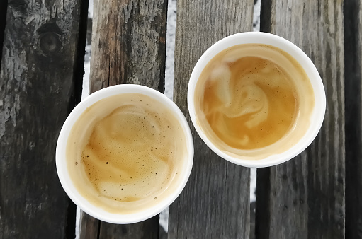 Two coffees with foam on a wooden bench, top view. Americano in paper cups on the street.