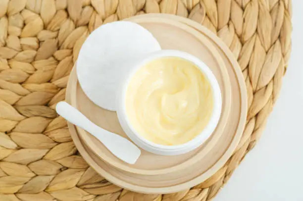 Yellow hair mask (banana face cream, shea butter mask, mango body butter) in a small white container. Natural skin care and hair treatment concept. Top view, copy space.