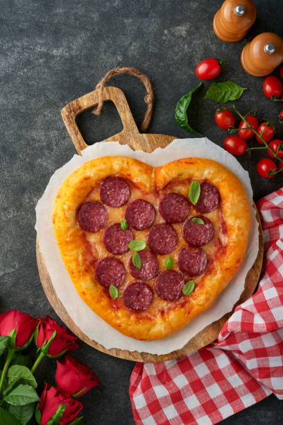 istock Valentines day heart shaped pizza with mozzarella, pepperoni and basil, wine bottle, two wineglass, gift box on black background. Idea for romantic dinner Valentines day. Top view. Mock up. 1464473417