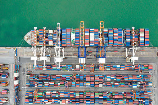 Aerial view Container ships at industrial ports in the business of import, export, logistics and international maritime transport, loading of containers on cargo ships with cranes,\nTransportation of goods by container trucks to customers.