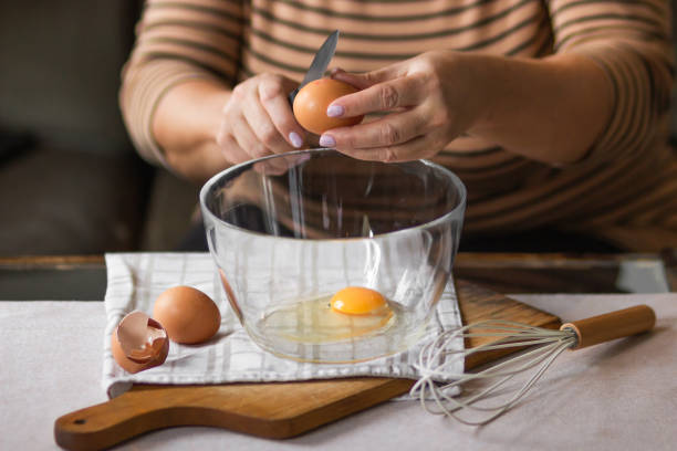 istock Old woman's hands cracking eggs into glass bowl with knife. Prepare for making omelet or pancakes for breakfast. 1464479705