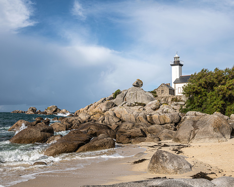 Lighthouse Pontusval Brittany France. Coast area with lighthouse, rocks, sea, waves and beach. Dramatic clouds in the sky.