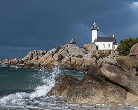 Lighthouse Pontusval Brittany France. Coast area with lighthouse, rocks, sea, waves and beach. Dramatic clouds in the sky.