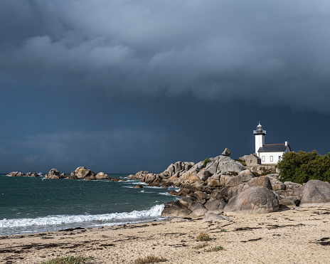 Lighthouse Pontusval Brittany France. Coast area with lighthouse, rocks, sea, waves and beach. Dramatic clouds in the sky.