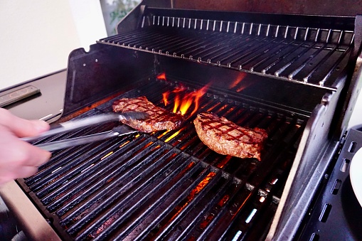 A man turns a steak on the grill. Two grilled steaks. Two pieces of meat on the fire. Barbecue and two pieces of meat. Grilled meat.