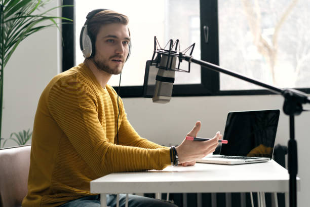 istock Man blogger smiling while broadcasting his live audio podcast in studio using headphones, laptop and headphones 1464484528