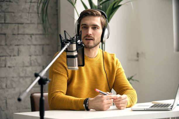 istock Man blogger smiling while broadcasting his live audio podcast in studio using headphones, laptop and headphones 1464484530