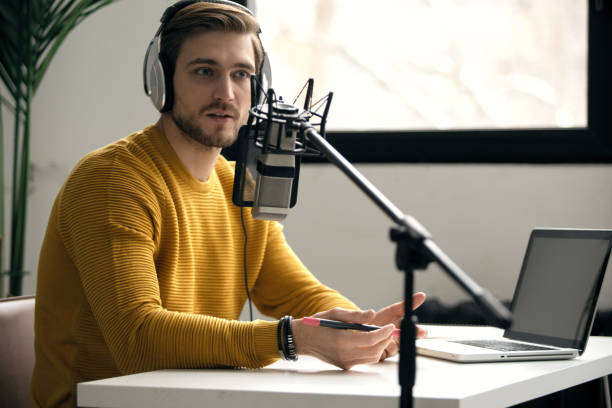 istock Man blogger smiling while broadcasting his live audio podcast in studio using headphones, laptop and headphones 1464484569