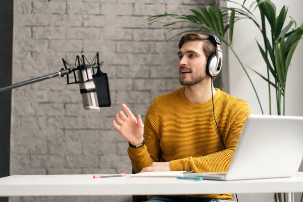 istock Man blogger smiling while broadcasting his live audio podcast in studio using headphones, laptop and headphones 1464484597