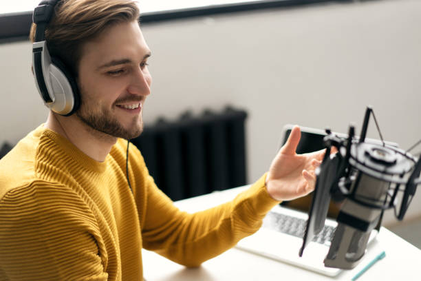 istock Man blogger smiling while broadcasting his live audio podcast in studio using headphones, laptop and headphones 1464484631