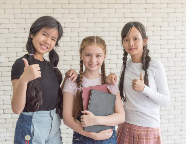 Three female students at an international school stand and thumb up\n.
