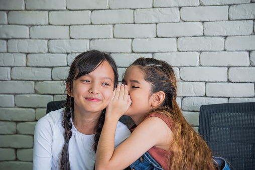 Two Asian female students whispering to each other inclassroom.