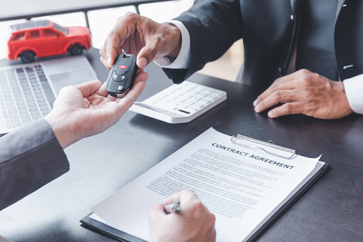 Concept of Car insurance or rental, salesman is making deal with buyer and giving key to him after sign sell contract or rental agreement.