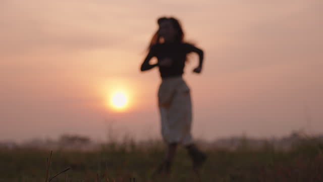 Blurry video for background of a woman running in a field during sunrise.